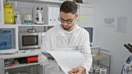 Photo for Focused man in labcoat analyzing documents in a modern laboratory setting - Royalty Free Image