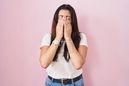 Jeune femme brune debout sur fond rose frottant les yeux pour la fatigue et les maux de tête, somnolent et l'expression fatiguée. problème de vision 
