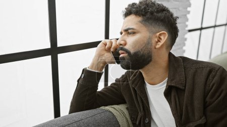 Téléchargez les photos : Beau jeune homme hispanique avec barbe parlant au téléphone à la maison - en image libre de droit