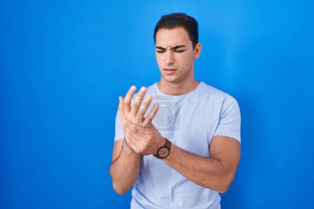 Photo for Young hispanic man standing over blue background suffering pain on hands and fingers, arthritis inflammation - Royalty Free Image