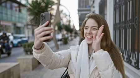 Téléchargez les photos : Une jeune femme joyeuse prenant un selfie dans une rue de la ville, soulignant la beauté urbaine, extérieure et la connectivité. - en image libre de droit