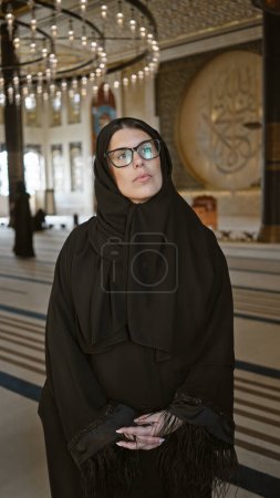 Foto de Una mujer contemplativa en hijab admira el interior adornado de una mezquita en doha, qatar, que encarna el turismo cultural. - Imagen libre de derechos
