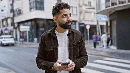 Junger hispanischer Mann mit Bart nutzt Smartphone auf Stadtstraße