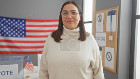 Hispanic senior woman smiling in a usa electoral center with american flags and vote banners