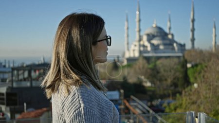 Foto de Una mujer contemplativa admira la icónica mezquita azul desde una terraza en Estambul, mostrando viajes y arquitectura. - Imagen libre de derechos
