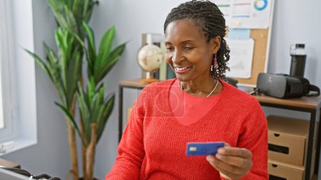 Foto de Una mujer afroamericana sonriente en una oficina con una tarjeta de crédito - Imagen libre de derechos