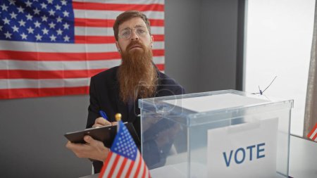 Téléchargez les photos : Un barbu avec des lunettes notant à côté d'une urne avec un fond de drapeau américain dans un bureau de vote. - en image libre de droit