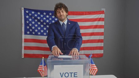 Bärtiger junger hispanischer Mann im Anzug, der bei einer amerikanischen Wahl mit uns Flaggen wählt