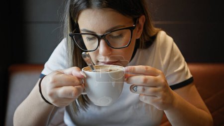 Photo for Hispanic adult woman enjoys a coffee at a cozy cafe, showcasing her stylish eyewear and casual attire. - Royalty Free Image