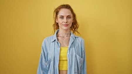 Foto de Una joven confiada en una chaqueta de mezclilla casual sobre un fondo amarillo vibrante posa para un retrato sincero. - Imagen libre de derechos