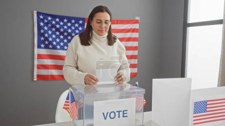 Hispanische Frau bei der Stimmabgabe in einem Wahllokal in den USA mit einer amerikanischen Flagge im Hintergrund