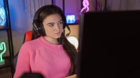 Photo for Focused young woman with headphones engages in gaming at home, showcasing a cozy, illuminated indoor environment. - Royalty Free Image