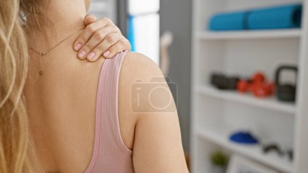 Photo for Young woman touching her shoulder in a physiotherapy clinic, suggesting recovery or pain management. - Royalty Free Image