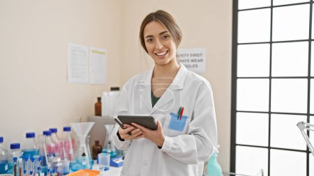 Lächelnde Wissenschaftlerin mit Tablette im Labor, umgeben von Geräten und Bechern