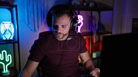 Téléchargez les photos : Un bel homme hispanique barbu portant un casque dans une salle de jeux éclairée au néon la nuit. - en image libre de droit