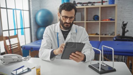 Middle-aged bearded man in lab coat using tablet at rehabilitation center clinic.