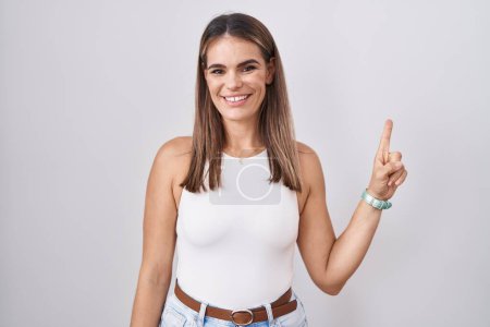 Photo for Hispanic young woman standing over white background showing and pointing up with finger number one while smiling confident and happy. - Royalty Free Image