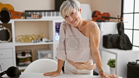 Photo for Portrait of a smiling middle-aged woman with short grey hair in a music studio surrounded by instruments. - Royalty Free Image