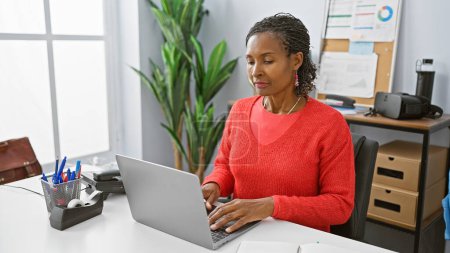 Photo for Focused african woman working on laptop in modern office interior. - Royalty Free Image