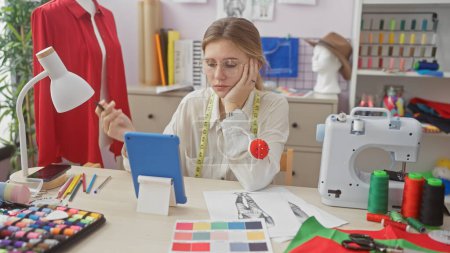 Téléchargez les photos : Une jeune femme concentrée sur le tailleur à l'aide d'une tablette dans un atelier coloré entouré d'équipements de couture. - en image libre de droit