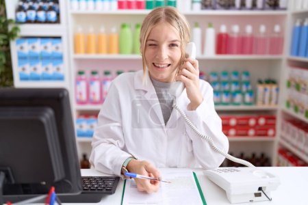 Téléchargez les photos : Jeune femme caucasienne travaillant à la pharmacie pharmacie parlant au téléphone clin d'oeil en regardant la caméra avec une expression sexy, gai et heureux visage. - en image libre de droit