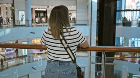 Foto de Mujer morena con vistas al bullicioso interior de un lujoso centro comercial dubai, que encapsula el consumismo y el estilo de vida urbano. - Imagen libre de derechos