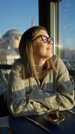 Photo for A contemplative woman enjoys tea at an istanbul restaurant with a view of the hagia sophia - Royalty Free Image