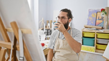 Photo for Handsome hispanic man drinking coffee in a bright art studio indoors - Royalty Free Image