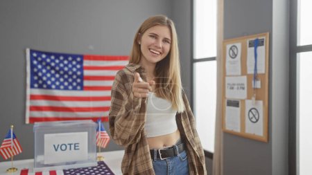 Blonde woman pointing at camera in a usa voting center with american flags