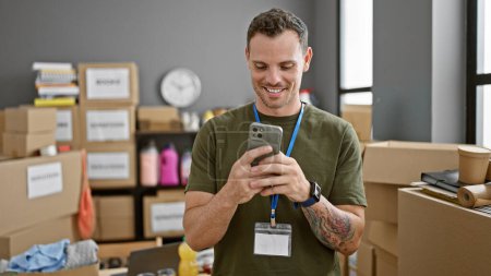 Photo for Smiling hispanic man with beard using smartphone in warehouse - Royalty Free Image