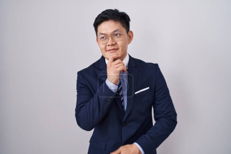 Photo for Young asian man wearing business suit and tie with hand on chin thinking about question, pensive expression. smiling and thoughtful face. doubt concept. - Royalty Free Image