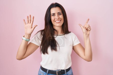Foto de Young brunette woman standing over pink background showing and pointing up with fingers number seven while smiling confident and happy. - Imagen libre de derechos