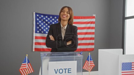 Mujer afroamericana confiada con brazos cruzados en un centro de votación, banderas y urnas visibles.