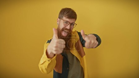 Photo for A happy man with a beard and glasses giving thumbs up against a yellow background. - Royalty Free Image