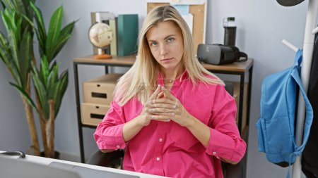 Téléchargez les photos : Femme blonde en chemise rose posant judicieusement à son bureau avec ordinateur. - en image libre de droit