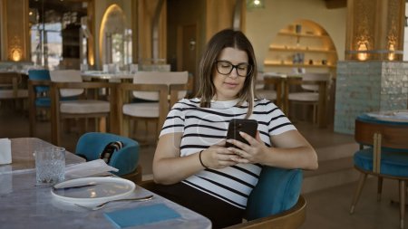 Téléchargez les photos : Jeune femme utilisant un smartphone dans un restaurant moderne, mettant en valeur la technologie, le mode de vie et l'ambiance gastronomique - en image libre de droit