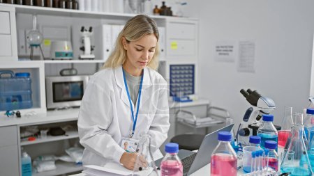Téléchargez les photos : Une jeune femme scientifique concentrée analysant des données sur un ordinateur portable dans un cadre de laboratoire moderne. - en image libre de droit