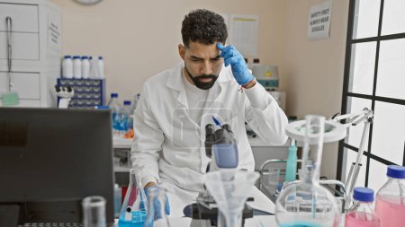 Foto de Un joven con bata de laboratorio exhibe concentración mientras trabaja en medio de equipos científicos en un laboratorio. - Imagen libre de derechos