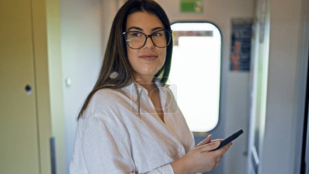 Téléchargez les photos : Jeune belle femme hispanique utilisant smartphone debout à l'intérieur du wagon de train - en image libre de droit
