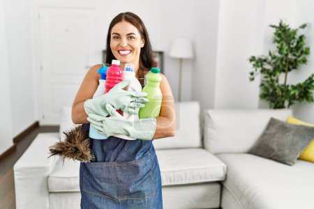 Foto de Joven hermosa mujer hispana sonriendo confiada sosteniendo productos limpios en casa - Imagen libre de derechos