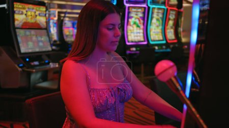 Foto de Una joven hispana adulta juega tragamonedas en un casino animado, evocando temas de juego, ocio y vida nocturna. - Imagen libre de derechos