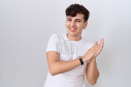 Téléchargez les photos : Jeune homme non binaire portant un t-shirt blanc décontracté applaudissant heureux et joyeux, souriant mains fières ensemble - en image libre de droit