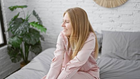 Téléchargez les photos : Femme caucasienne souriant dans une chambre moderne avec un lit et une plante en arrière-plan, exsudant une élégance décontractée - en image libre de droit