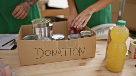 Photo for A woman and a man volunteer in a warehouse arranging canned food and bottled juice donations. - Royalty Free Image
