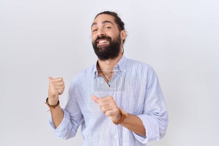Téléchargez les photos : Homme hispanique avec la barbe portant chemise décontractée pointant vers le dos derrière avec la main et les pouces vers le haut, souriant confiant - en image libre de droit