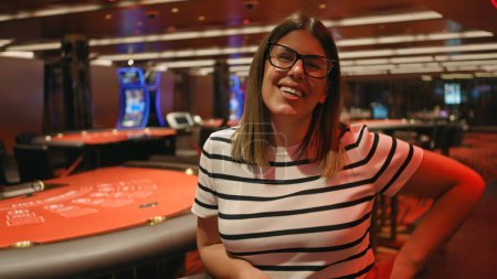 Foto de Mujer joven sonriente con gafas en la mesa del casino, que encarna ocio, entretenimiento y juegos de azar. - Imagen libre de derechos