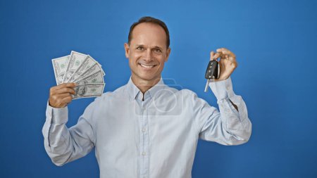 Photo for Joyful middle age hispanic man smiling broadly, holding key to his new car and wads of dollars, representing wealth and financial success, isolated on a white background - Royalty Free Image