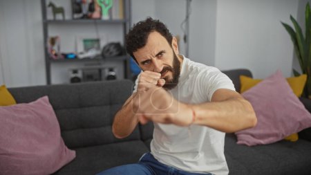 Photo for Middle-aged bearded man in white shirt boxing indoors, displaying fitness and activity in a home setting. - Royalty Free Image