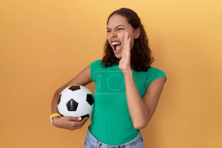 Téléchargez les photos : Jeune femme hispanique tenant le ballon criant et criant fort à côté avec la main sur la bouche. concept de communication. - en image libre de droit