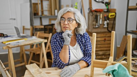 Foto de Una mujer reflexiva en un taller rodeado de herramientas de carpintería y madera. - Imagen libre de derechos